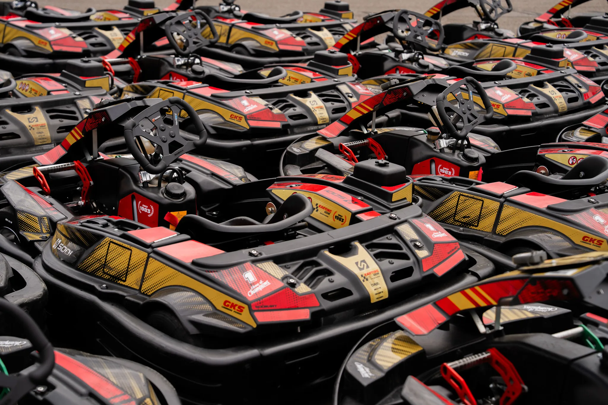Rijen rood-gouden Sodi-karts van Karting Genk staan klaar in de paddock.
